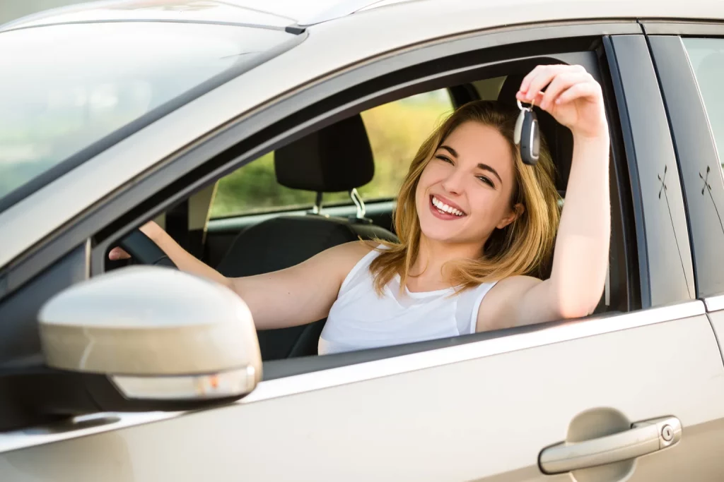 Young woman in new car holding keys after she secured first car loan