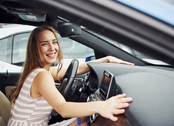 A young female touching the dash of her car, happy she has been approved for a car loan